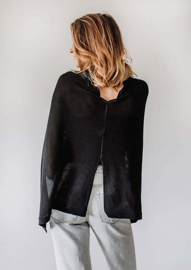 Back view of Emily Baldoni in a black knit Cocoon nursing cover worn as a cape with metallic black piping 