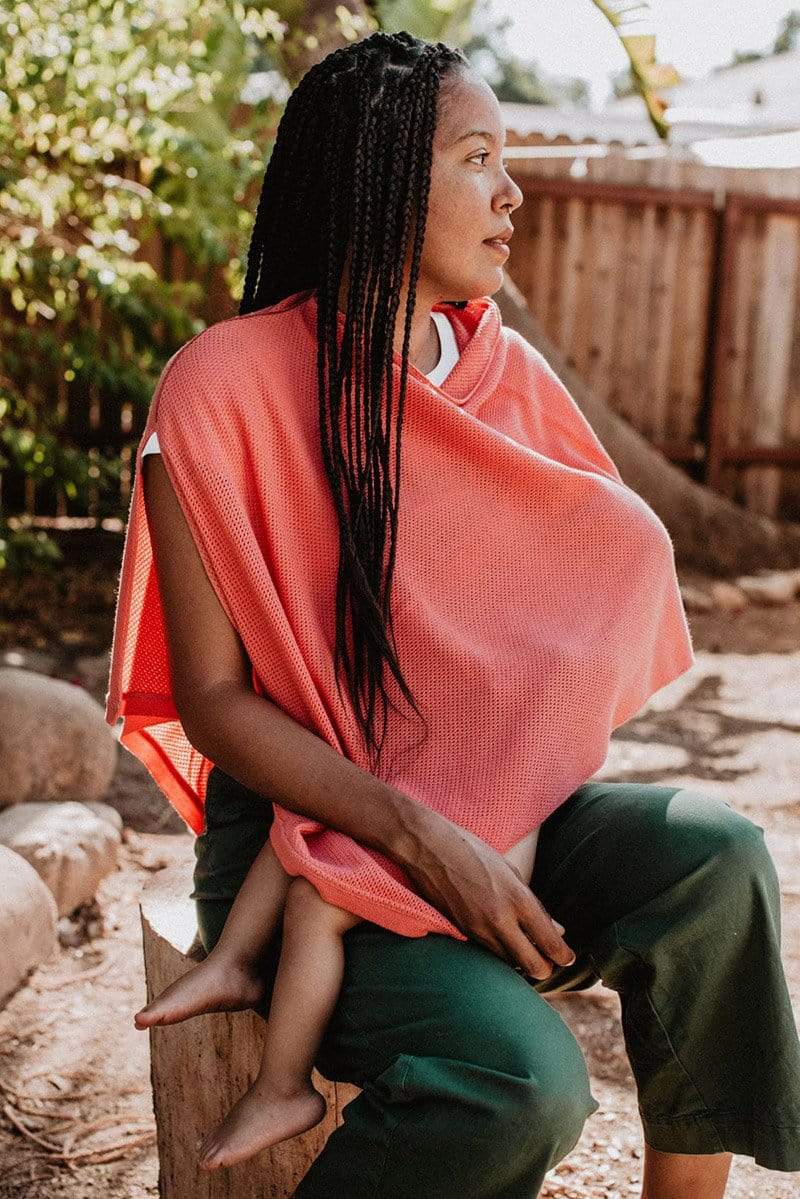 Black woman with braids breastfeeding in coral knit Cocoon nursing poncho