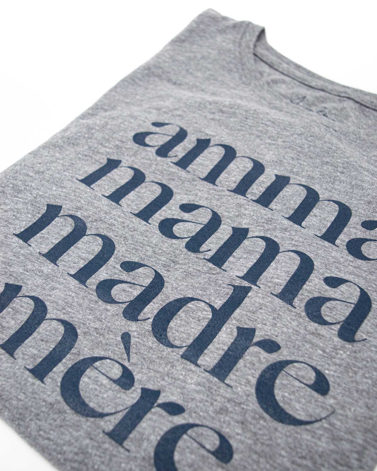 Folded heather grey tee shirt that reads Amma, Mama, Madre, Mere on a white background