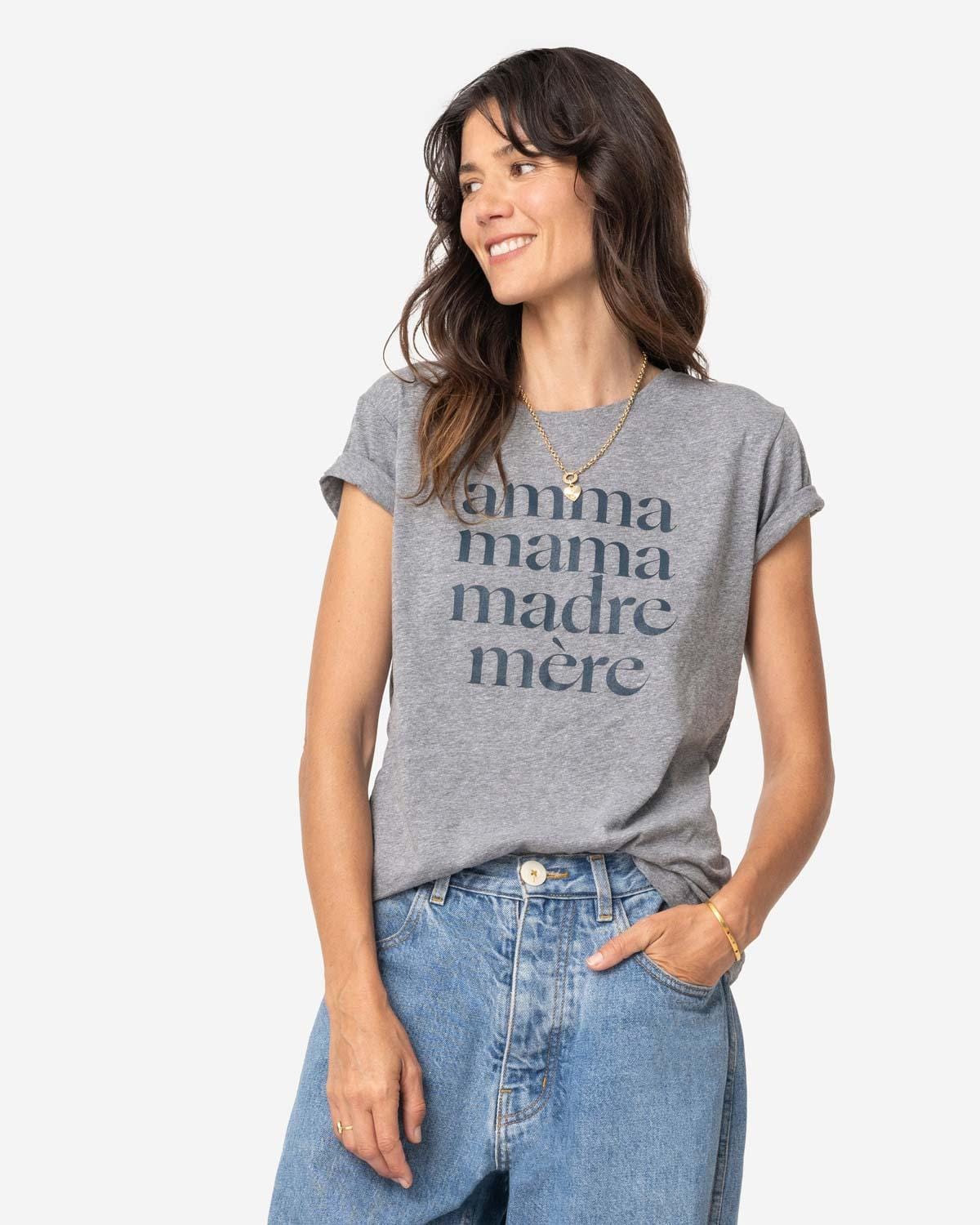 Young mom with long brown hair wearing loose jeans and a heathered grey tee shirt that reads Amma, Mama, Madre, Mere in size S on a white background