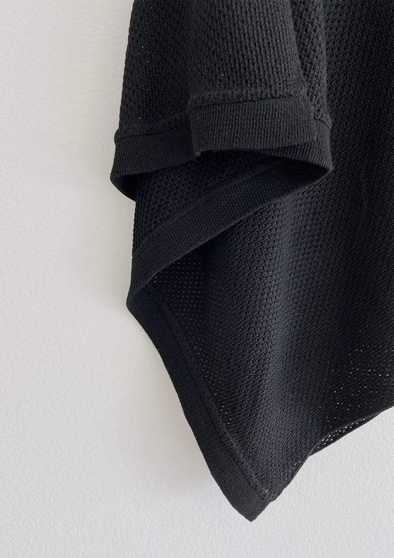 Closeup of black knit Cocoon nursing cover showing breathable texture of knit and straight edge hem against white background