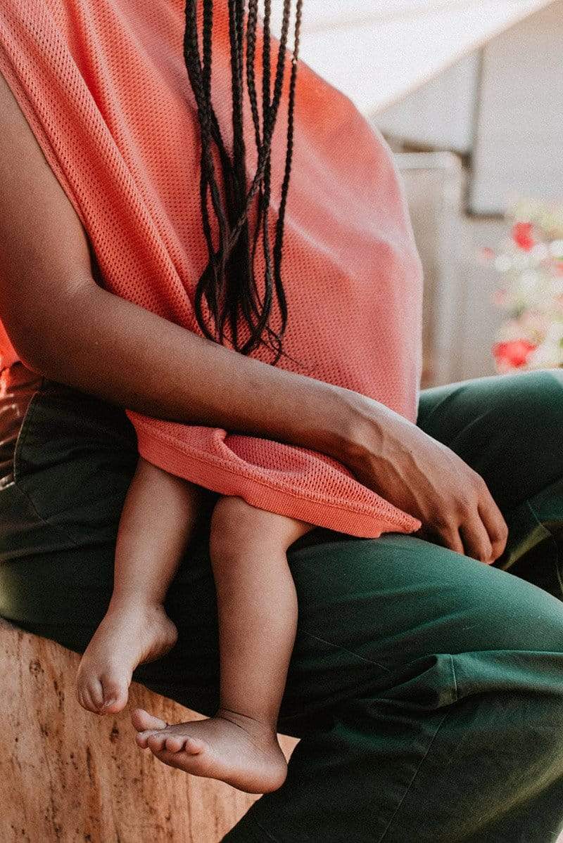 Closeup of Black woman with braids breastfeeding in coral knit Cocoon nursing poncho 